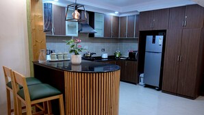 Een moderne keuken met donkerhouten kasten, een centraal eiland met krukken, een roestvrijstalen koelkast en een hanglamp.