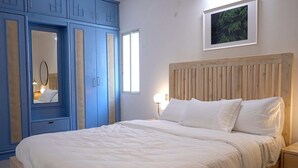 Een slaapkamer met een groot bed, een houten hoofdbord, een nachtkastje, een bedlampje en een kledingkast met spiegel.