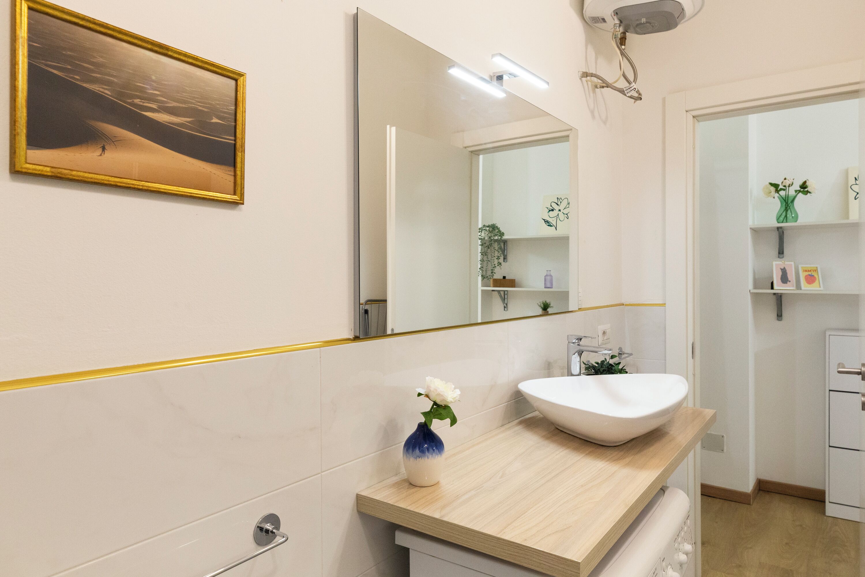 A modern bathroom with a large mirror, a white sink, and a vase with a single flower.