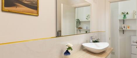 A modern bathroom with a large mirror, a white sink, and a vase with a single flower.