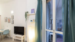 A modern living room with a flat-screen TV, a small table, and a chair. There is a window with curtains, a potted plant, and framed pictures on the wall. - notaMI - Welcome Darsena (Milan)