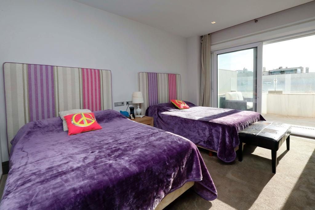 A hotel room with two beds, a small table, and a view of the city through a large window.