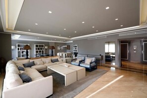 A spacious living area with a large sectional sofa, a smaller sofa, and a coffee table. There are built-in shelves and a fireplace in the background.
