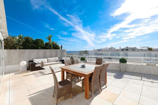 A rooftop terrace with a dining table and chairs, a sofa, and a view of the cityscape.