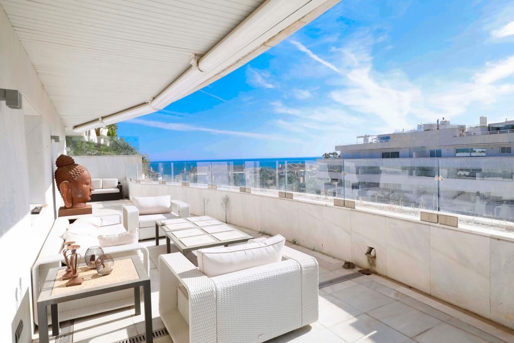 Une terrasse sur le toit, dotée de mobilier en osier blanc, d’une statue de Bouddha et offrant une vue dégagée sur les toits de la ville et l’océan.