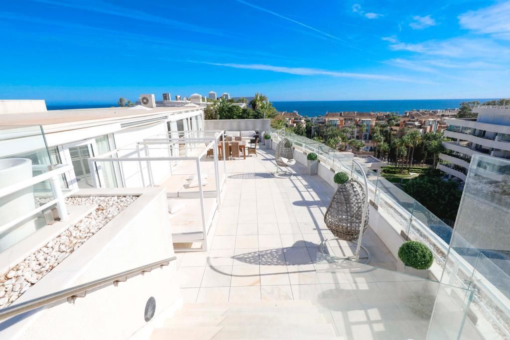 A rooftop terrace with a clear view of the sea, outdoor seating, and modern architecture.