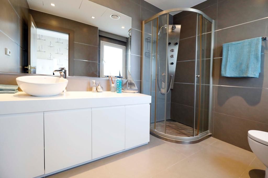 Et moderne badeværelse med en stor hvid vask, en brusekabine med glasvægge og et toilet.