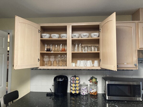 Una cocina con un mueble que contiene distintos vasos y una cafetera sobre la encimera.