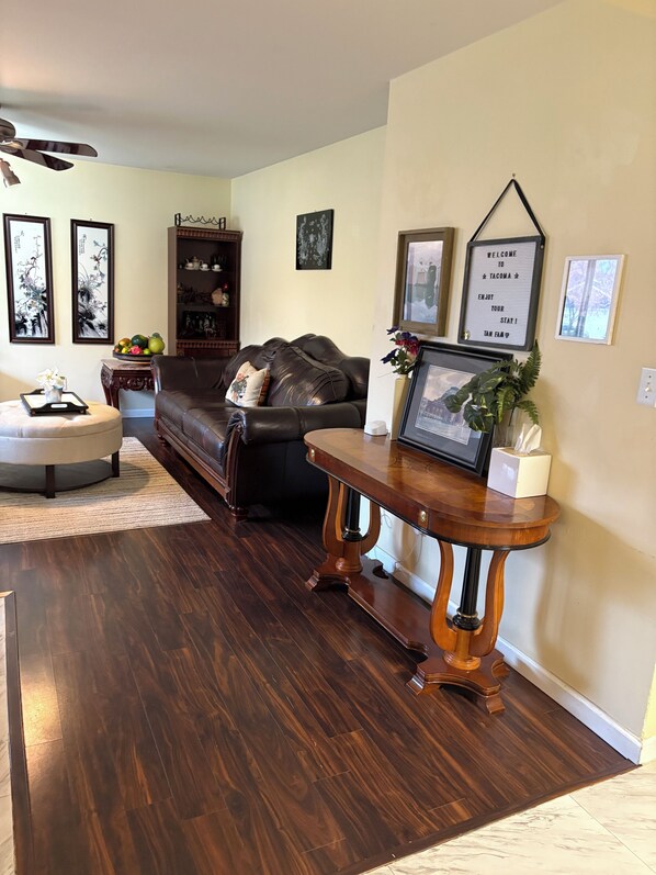 A living room with a dark wood floor, a leather sofa, a wooden coffee table, and a wall-mounted sign. - Fantastic 4-bedroom house with AC in charming Tacoma, the heart of Puget Sound. (Tacoma)