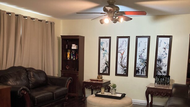 A living room with a dark wood floor, a leather sofa, a round ottoman, a coffee table, and a ceiling fan. There are framed artworks on the wall and a small side table with a vase. - Fantastic 4-bedroom house with AC in charming Tacoma, the heart of Puget Sound. (Tacoma)