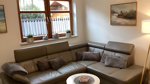 Un salon avec un canapé en cuir marron, une table basse ronde et un tableau accroché au mur.