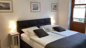 Un lit double avec du linge de lit blanc et deux oreillers, une table de chevet avec une lampe, et des tableaux encadrés au mur.