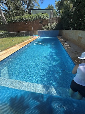 A rectangular swimming pool with a clear blue water surface, surrounded by a wooden deck and a brick wall. - Villa Palmera a-resort style house, close to amenities, transpor, shopping, city (Lindfield)