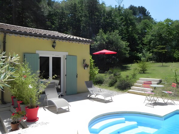 Un bâtiment jaune avec une piscine, des sièges à l’extérieur et un parasol rouge.