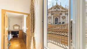 A hotel room with a wooden floor, a view of a historic building through a window, and a curtain. - Casa Colonna, a Burghesius home (Roma)