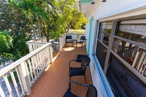 Une terrasse en bois avec une balustrade blanche, deux fauteuils en osier et une table avec des chaises.