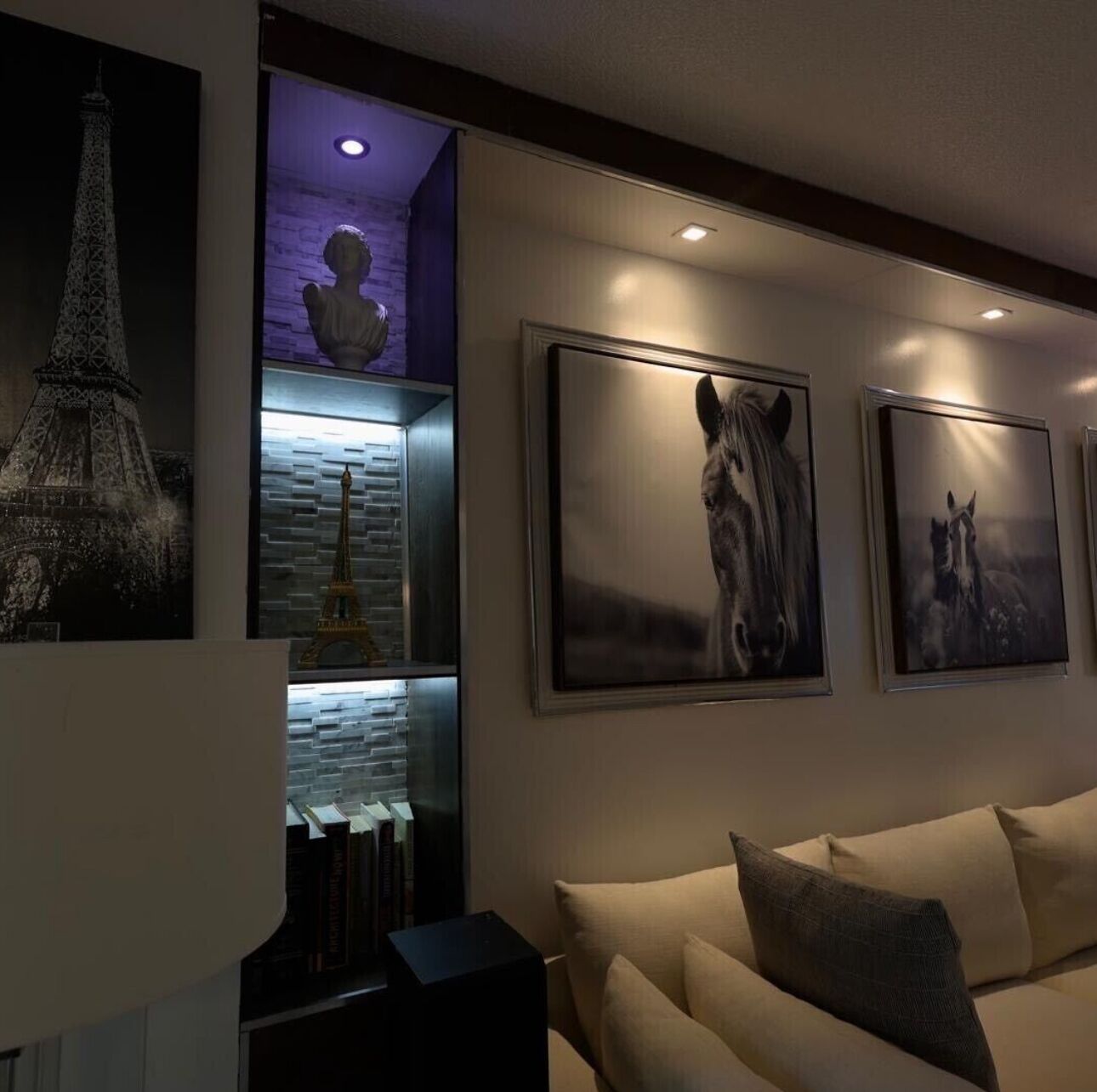 Una sala de estar moderna con un sofá, una estantería y obras de arte enmarcadas en la pared.