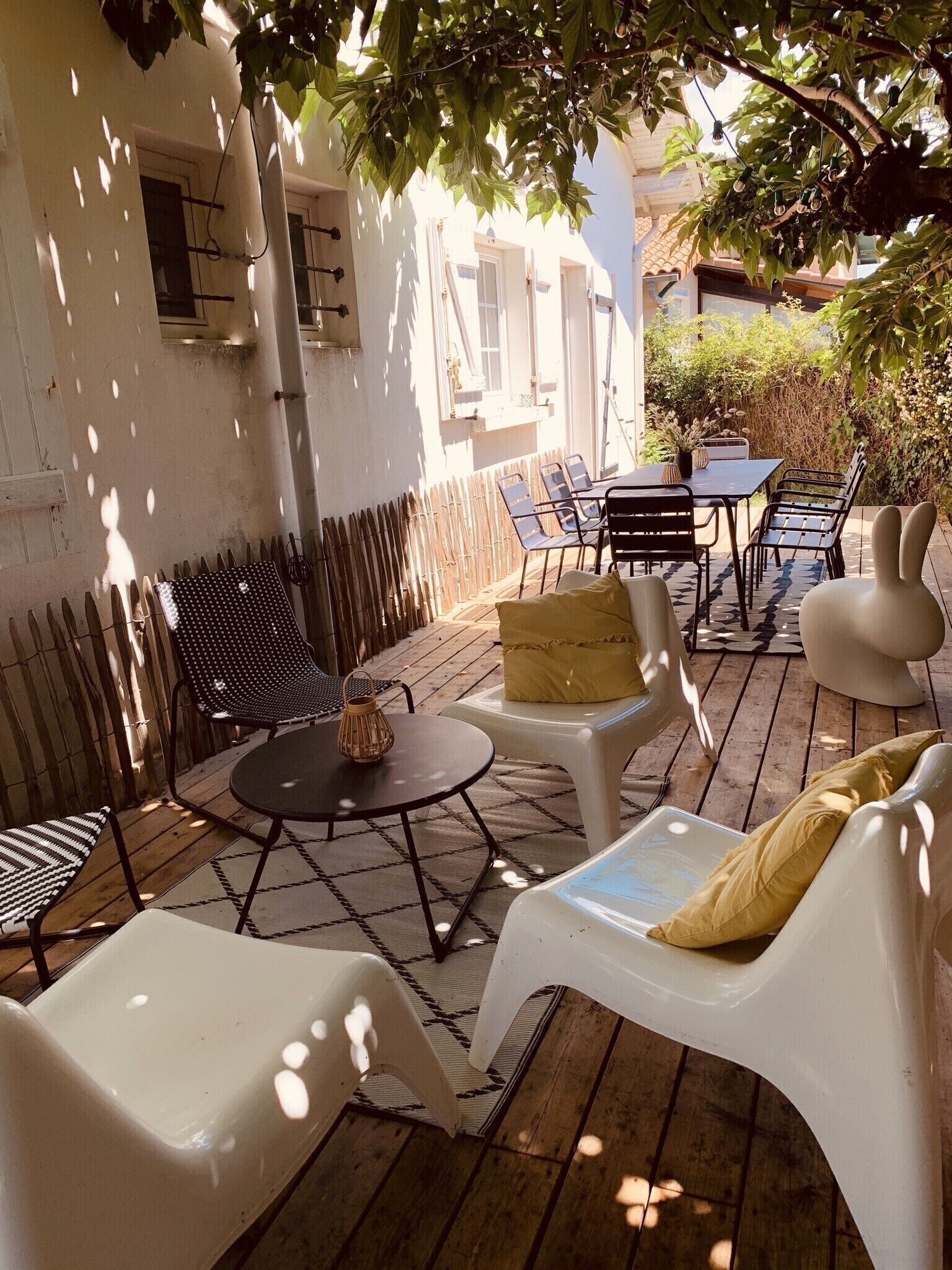 An outdoor patio with a table and chairs, a white wall, and a wooden fence.