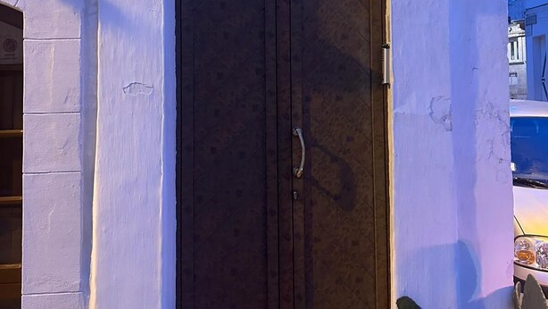 Eine dunkle Holztür mit Griff, eingebettet in ein weißes, rundbogenförmiges Portal, das von weißen Säulen gesäumt wird, mit einer Nummer '20' als Schild darüber.