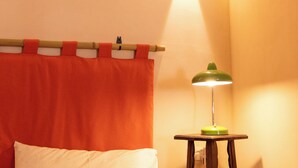 Ein Zimmer mit Steindecke, einem Bett mit orangefarbenem Kopfteil und einer grünen Tischlampe.
