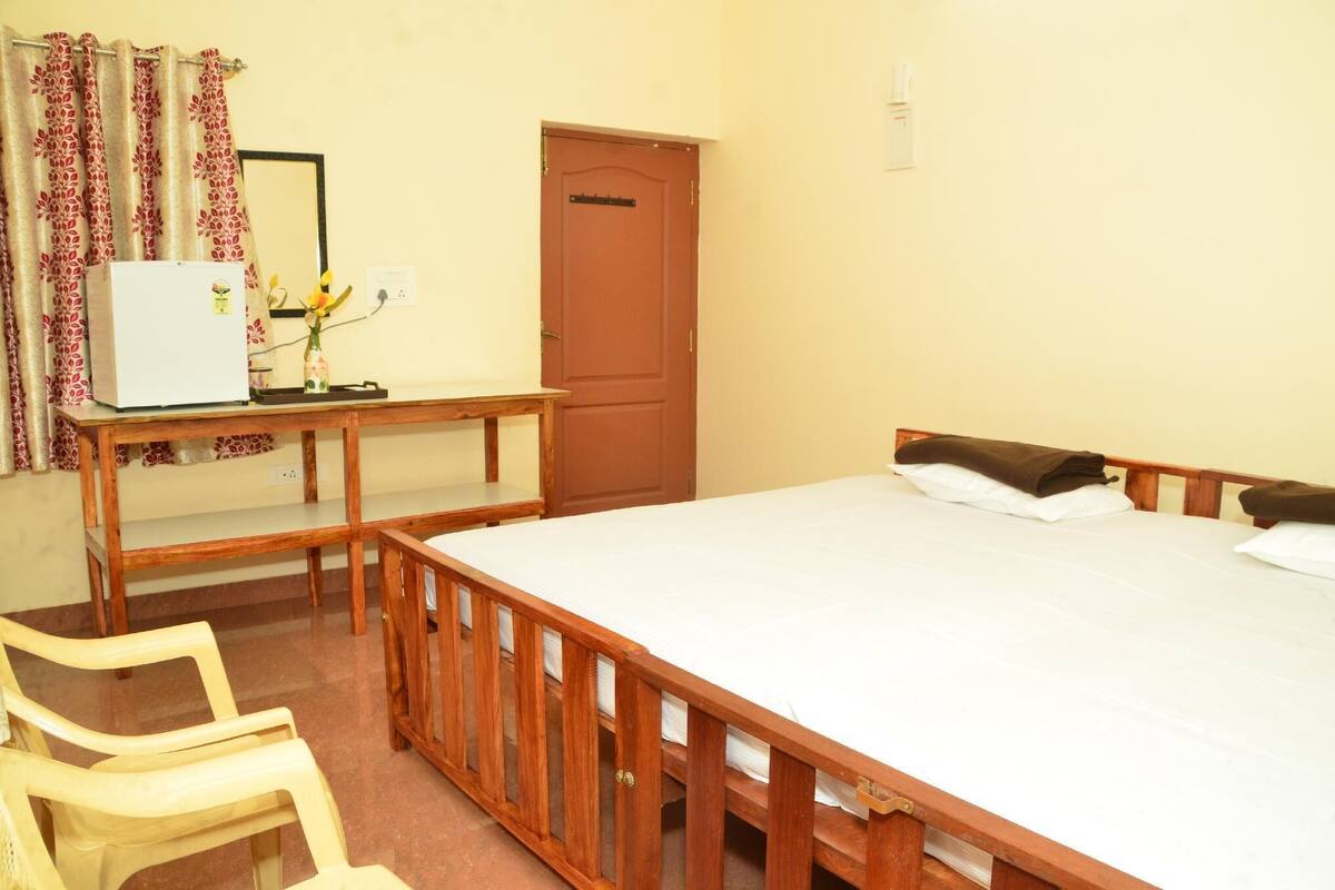 Een slaapkamer met een houten bed, een klein bureau met een koelkast en een stoel.