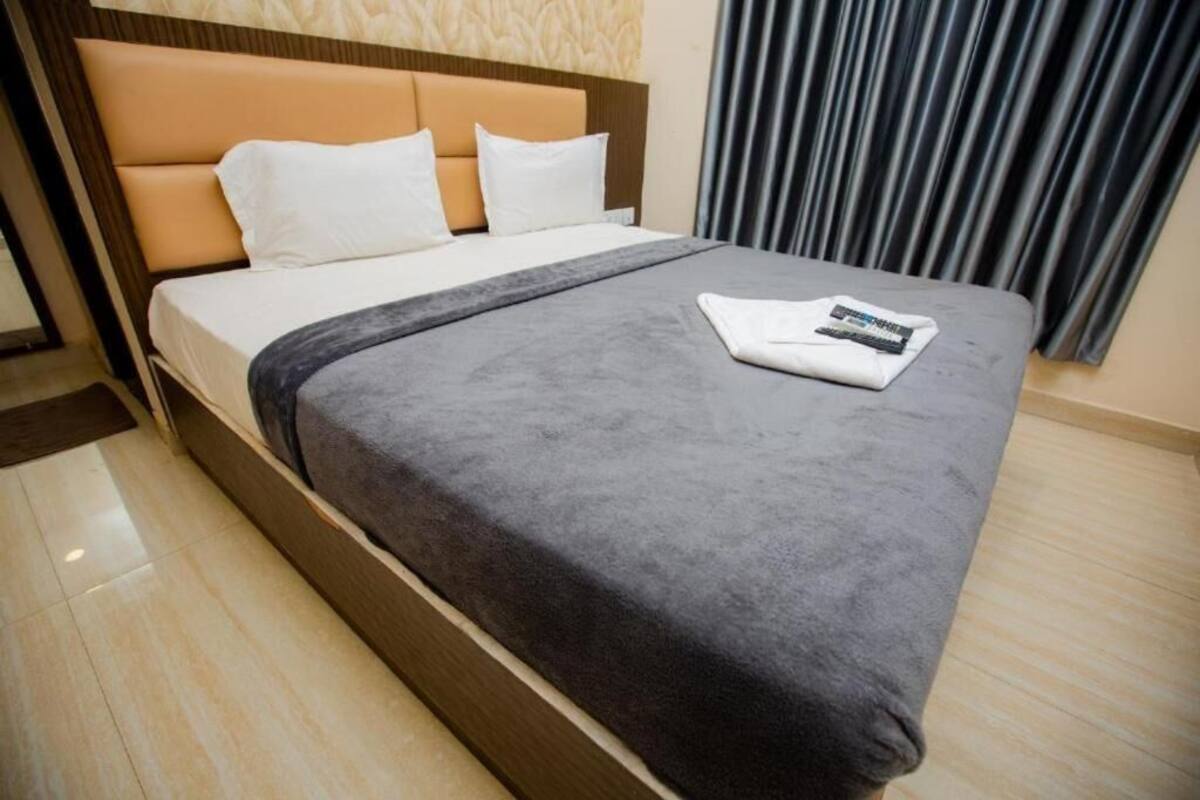 A neatly made bed with a grey blanket and white pillows, a remote control on the bed, and a wooden headboard.