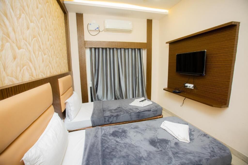 A hotel room with two beds, a TV mounted on a wooden panel, and an air conditioning unit on the wall.