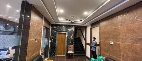 A hotel lobby with a reception desk, seating area, and a staircase leading to other floors.