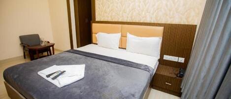 Una habitación de hotel con una cama grande, una mesita de noche, una silla y una cortina.