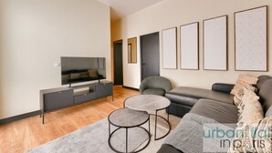 Ein modernes Wohnzimmer mit Flachbildfernseher, einer Couch, einem Couchtisch und gerahmten Kunstwerken an der Wand.