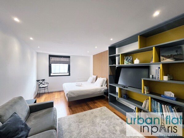 Un dormitorio moderno con cama, sofá, estantería y ventana.