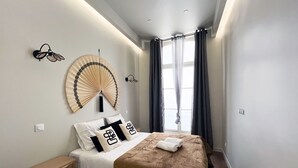 Ett modernt hotellrum med en säng, ett sängbord och ett stort fönster med gardiner.