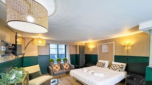 Hotellihuone, jossa on sänky, sohva, pieni pöytä, televisio ja suuri ikkuna.