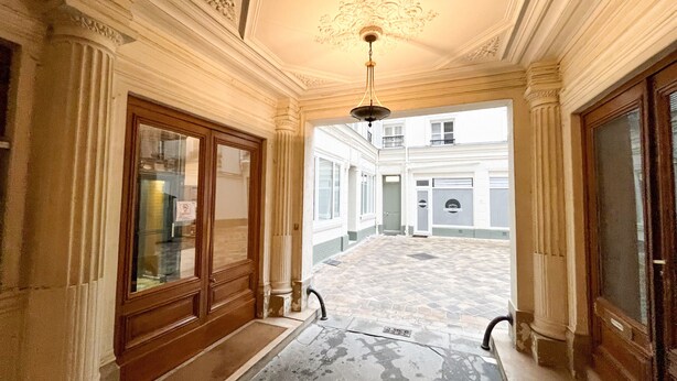 Un pasillo con techo ornamentado y columnas, que conduce a un patio con una fuente.