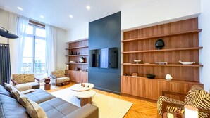Una sala de estar moderna con un sofá, sillones, una mesa de centro y estanterías de madera con objetos decorativos.