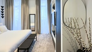 Una habitación de hotel moderna con una cama grande, un banco, un espejo y un televisor montado en la pared.