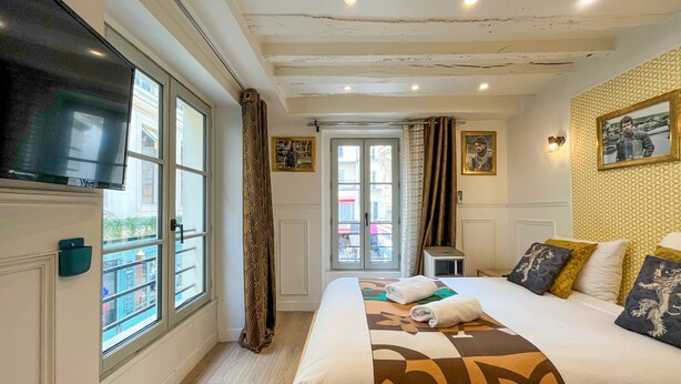 Una habitación de hotel con una cama, televisión, ventana y puerta que da a un balcón.