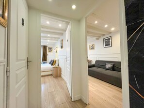 A hallway leading to a bedroom with a bed, a bedside table, and a dresser. There is a dark-colored sofa in the adjacent room. - Urban Flat 42 - Game of Thrones Apartment Paris (París)