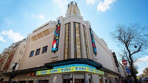 Un teatro histórico con un diseño arquitectónico clásico, que cuenta con un cartel llamativo y una estatua en la parte superior.