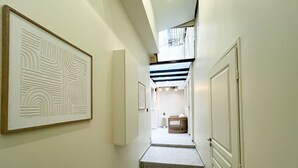 Un couloir avec un escalier menant à un balcon situé au deuxième étage, des œuvres d’art encadrées accrochées aux murs et un petit coin salon avec une table et des chaises.