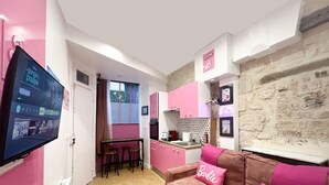 Eine kleine Küche mit rosa Schränken und einer Steinwand. Ein Barhocker-Set befindet sich in der Nähe der Küchenarbeitsplatte, sowie ein kleiner Esstisch.