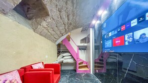 Ein modernes Interieur mit einem roten Sofa, einer rosa Treppe und einem Fernseher, der Fernsehsenderlogos zeigt.