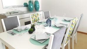 A dining table set with plates, cutlery, and glasses, surrounded by chairs with cushions. - Modern Apartment with Ocean View | Right on the Beach at Praia da Rocha (Faro)