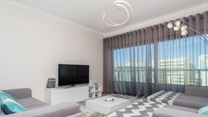 Een moderne woonkamer met een flatscreen televisie, grijze banken, een witte salontafel en een vloerkleed met een patroon.