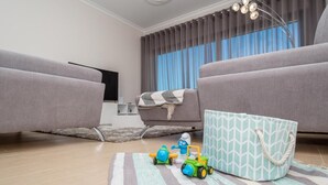Een moderne woonkamer met twee grijze banken, een gestreept vloerkleed en kinderspeelgoed op de vloer.