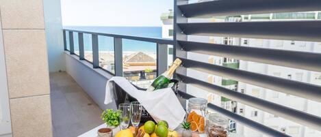 Un balcon avec une table dressée, ornée de fruits, d’une bouteille de champagne et d’un verre.