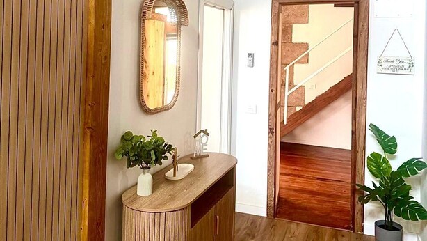 Eine Holztreppe führt zu einer zweiten Etage, ein Spiegel in Holzleiste, ein Holzschminktisch mit Pflanze und eine Pendelleuchte.