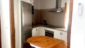 Eine kleine Küche mit Holztischplatte, zwei weißen Barhocker, einem Edelstahlkühlschrank und einem Einbauofen.