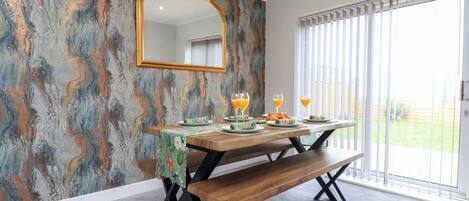 Un comedor con una pared con diseño de mármol, una mesa de madera con bancos y un amplio ventanal con persianas.