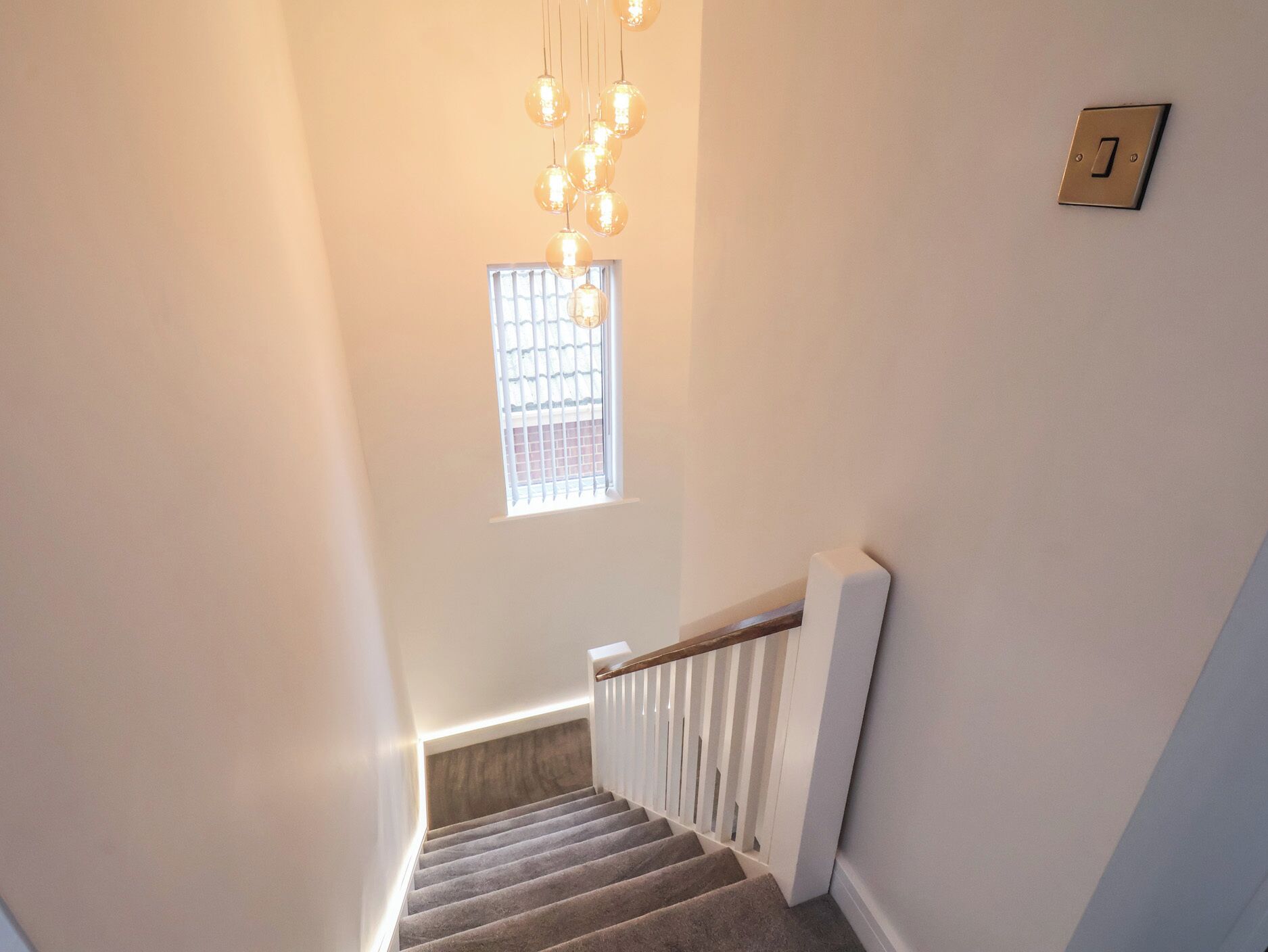 A staircase with a handrail, a light switch, and a window with bars.